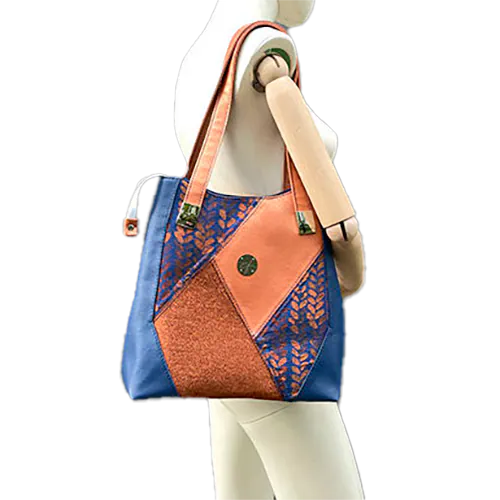 A shoulder bag made up of a patchwork of different materials: royal blue faux leather, golden faux leather, shiny bronze fabric, and blue and bronze wrap fabric with a pattern of small droplets.