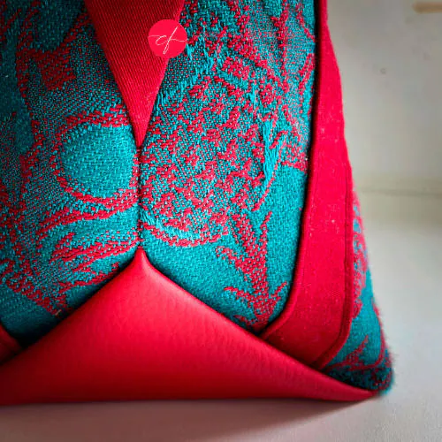 A shoulder bag made from blood red and emerald green babywearing wrap with a thistle pattern, red gabardine, emerald green linen, and synthetic material.