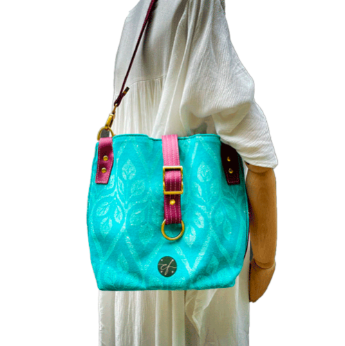 A shoulder bag made of turquoise and ecru babywearing wrap with a leaf pattern, plum synthetic leather, and iridescent mint poplin.