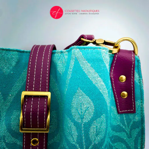 A shoulder bag made of turquoise and ecru babywearing wrap with a leaf pattern, plum synthetic leather, and iridescent mint poplin.