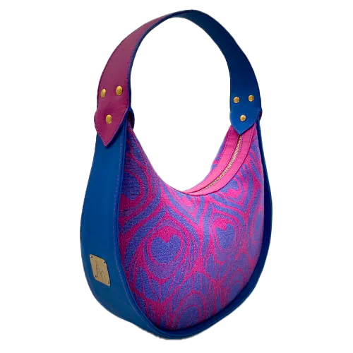 A shoulder bag made from royal blue and bright pink leathers, combined with a pink and blue baby wrap fabric featuring stylized peacock feather motifs.
