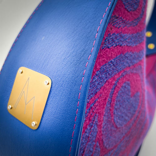 A shoulder bag made from royal blue and bright pink leathers, combined with a pink and blue baby wrap fabric featuring stylized peacock feather motifs.