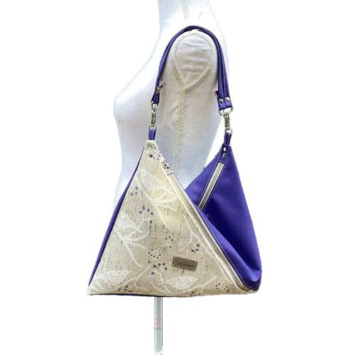 A triangular shoulder bag made of beige synthetic leather and white, cream, beige, and green babywearing fabric.