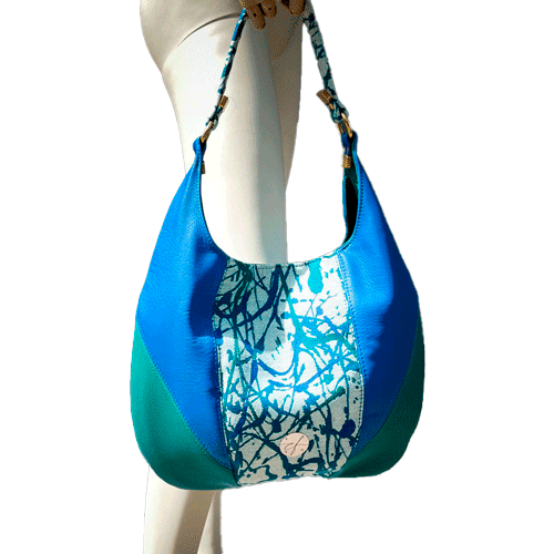 A shoulder bag made of royal blue and sage green leather, white, blue, and green babywearing fabric with an organic pattern, and fir green poplin.