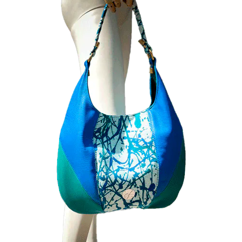A shoulder bag made of royal blue and sage green leather, white, blue, and green babywearing fabric with an organic pattern, and fir green poplin.