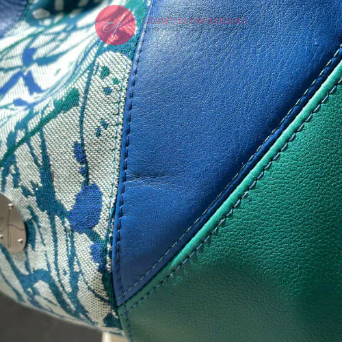 A shoulder bag made of royal blue and sage green leather, white, blue, and green babywearing fabric with an organic pattern, and fir green poplin.