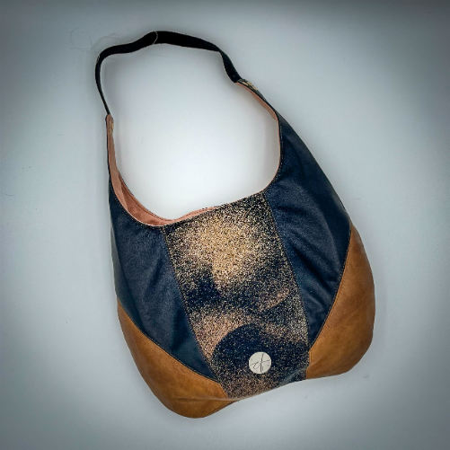 A shoulder bag made of brown and black leathers, a black, brown, and beige babywearing wrap with a round abstract pattern, and peach linen canvas.