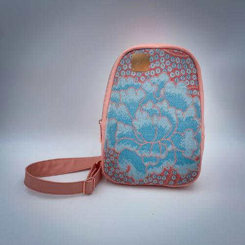 A backpack made of peach-colored faux leather and a babywearing wrap in shades of pink and turquoise with a vintage floral pattern.
