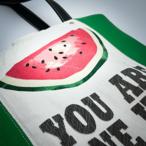 A large bag made from green leather on the outside and a canvas printed with a fruit design with an English pun underneath, and on the inside a forest green poplin.