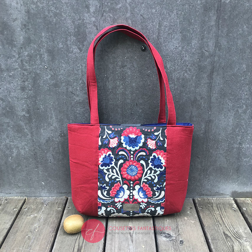 A tote bag made from gray fabric embroidered with blue, red, and white Scandinavian floral motifs, red gabardine, and royal blue poplin.