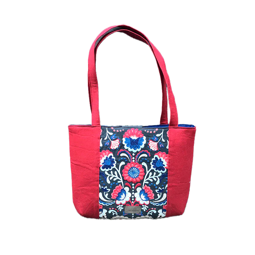 A tote bag made from gray fabric embroidered with blue, red, and white Scandinavian floral motifs, red gabardine, and royal blue poplin.