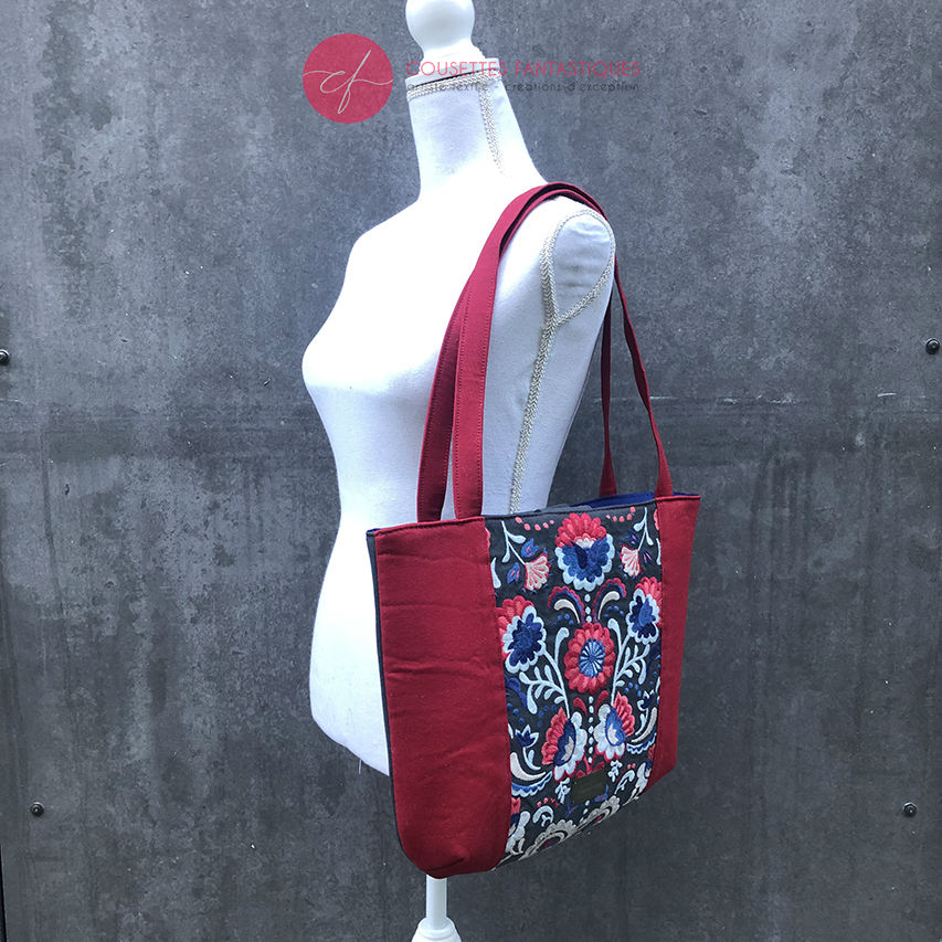 A tote bag made from gray fabric embroidered with blue, red, and white Scandinavian floral motifs, red gabardine, and royal blue poplin.