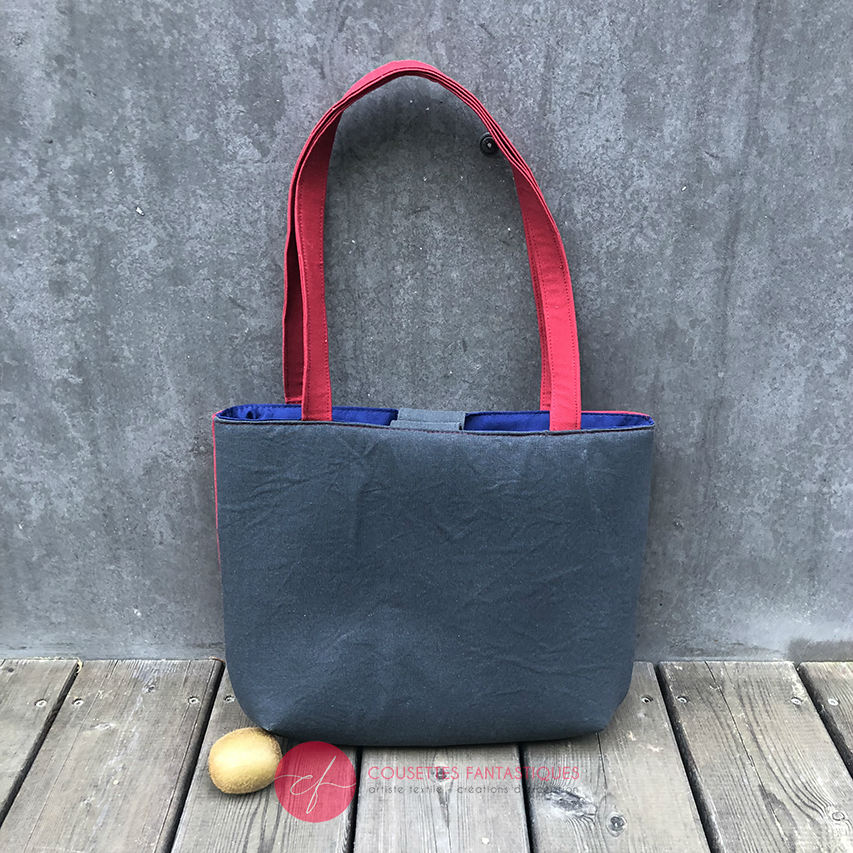 A tote bag made from gray fabric embroidered with blue, red, and white Scandinavian floral motifs, red gabardine, and royal blue poplin.