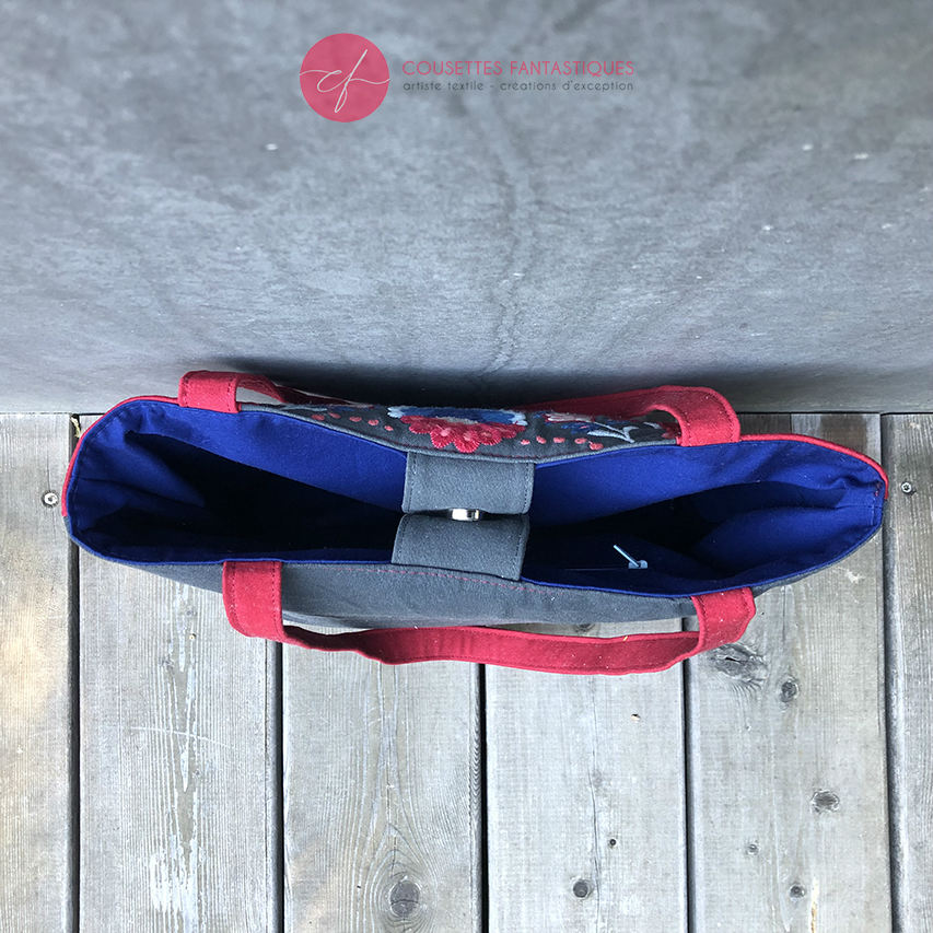 A tote bag made from gray fabric embroidered with blue, red, and white Scandinavian floral motifs, red gabardine, and royal blue poplin.