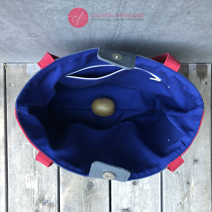 A tote bag made from gray fabric embroidered with blue, red, and white Scandinavian floral motifs, red gabardine, and royal blue poplin.