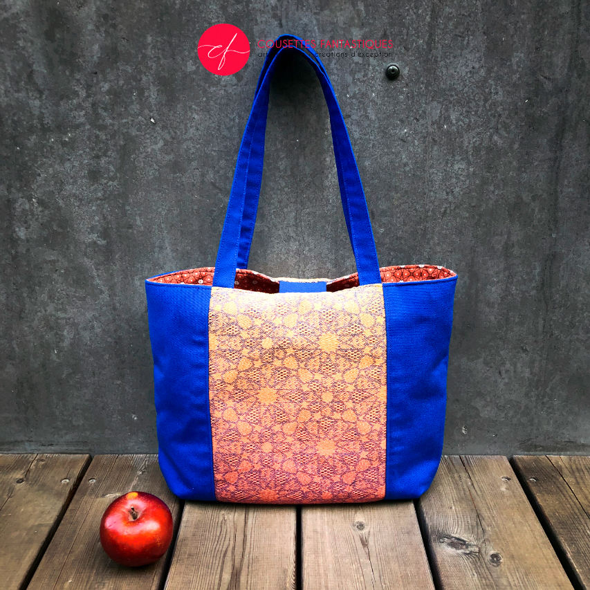 A tote bag made from royal blue fabric, a babywearing wrap with an Arabesque geometric pattern in blue on a gradient background from orange to yellow, and orange cretonne with geometric patterns.