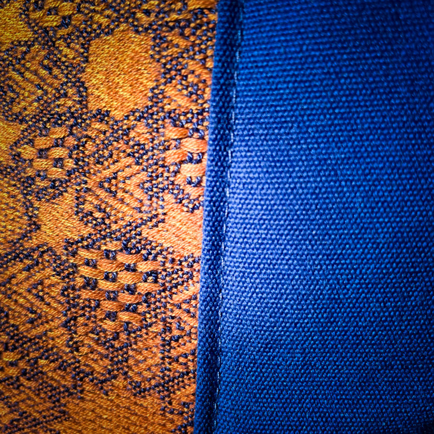 A tote bag made from royal blue fabric, a babywearing wrap with an Arabesque geometric pattern in blue on a gradient background from orange to yellow, and orange cretonne with geometric patterns.