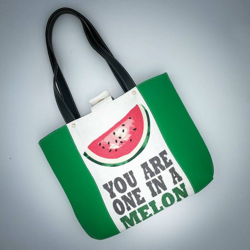 A large bag made from green leather on the outside and a canvas printed with a fruit design with an English pun underneath, and on the inside a forest green poplin.