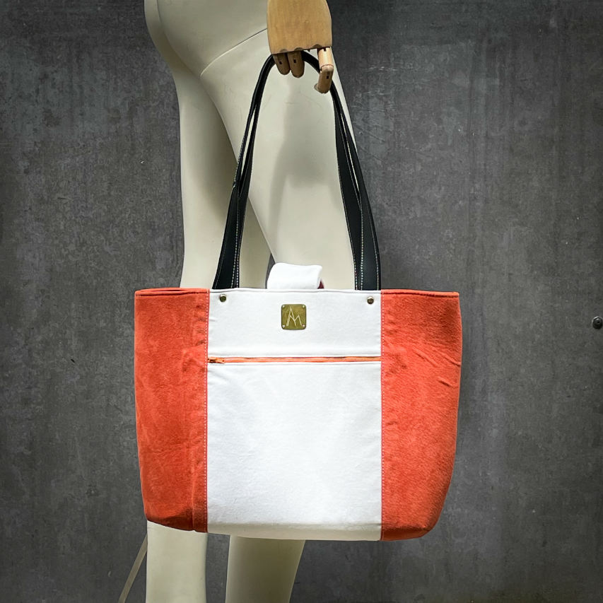 A large bag made from orange leather on the outside and a canvas printed with a fruit design and English wordplay underneath, with an iridescent orange viscose interior.