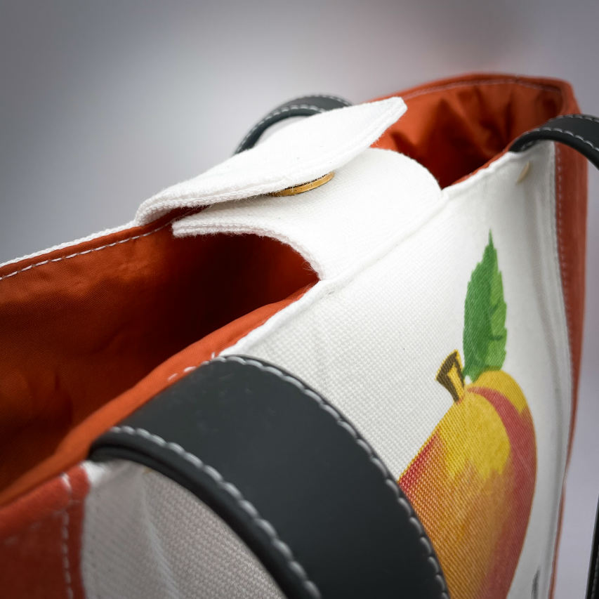 A large bag made from orange leather on the outside and a canvas printed with a fruit design and English wordplay underneath, with an iridescent orange viscose interior.