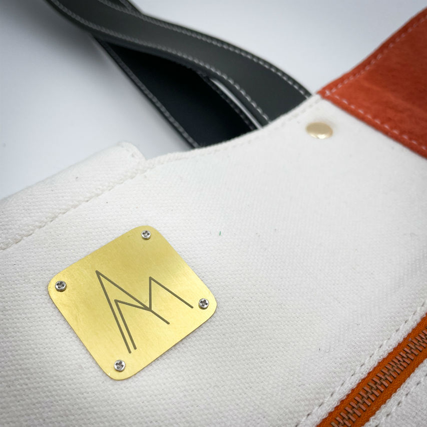 A large bag made from orange leather on the outside and a canvas printed with a fruit design and English wordplay underneath, with an iridescent orange viscose interior.