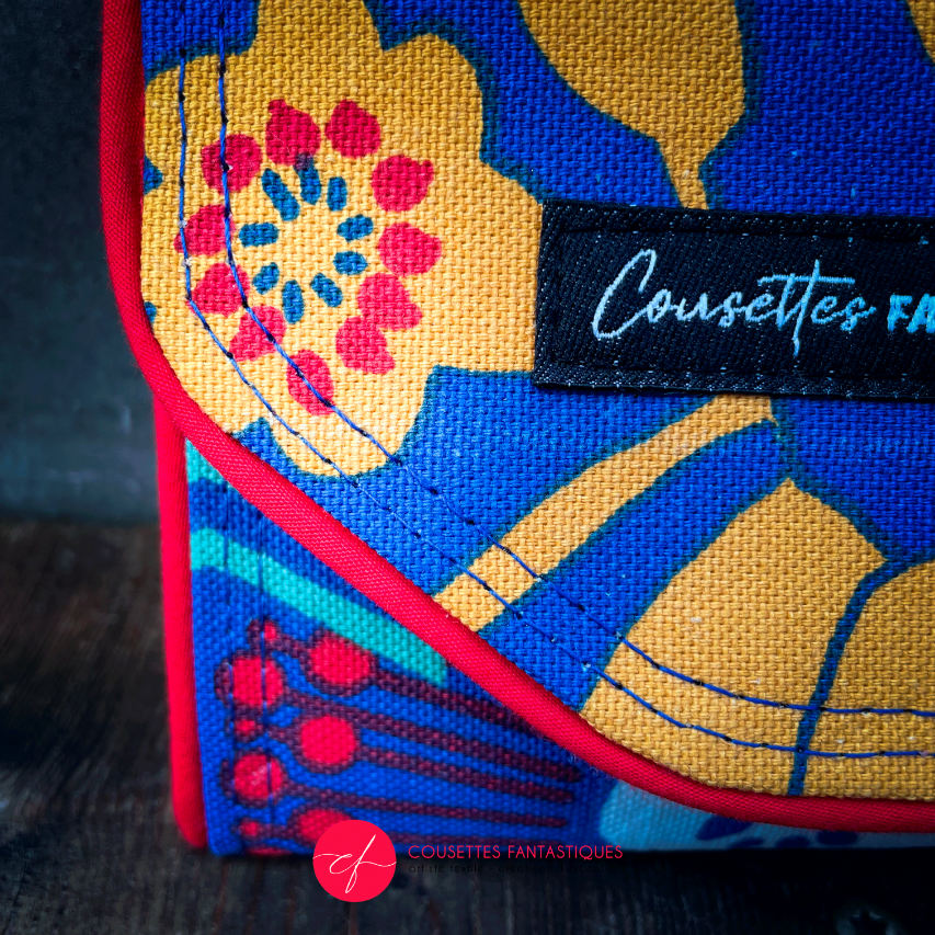 A wallet made from royal blue fabric with yellow, white, and red floral patterns on the outside and plain yellow and red fabrics on the inside.