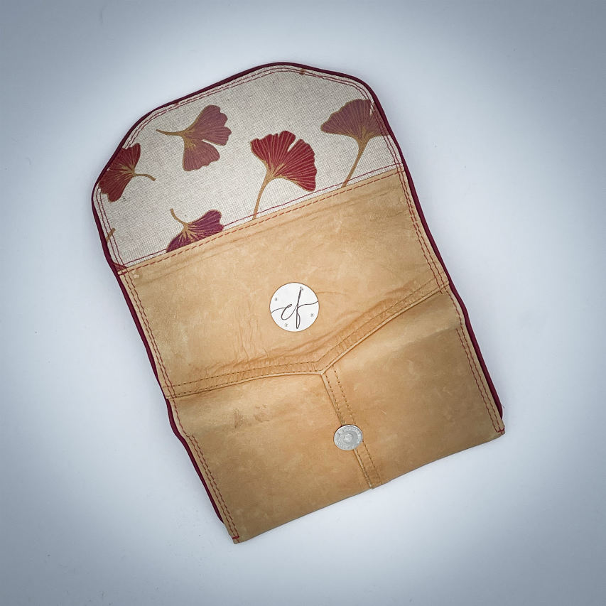 A wallet made from camel colored leather and a red Ginkgo Biloba leaves patterned polycotton canvas.