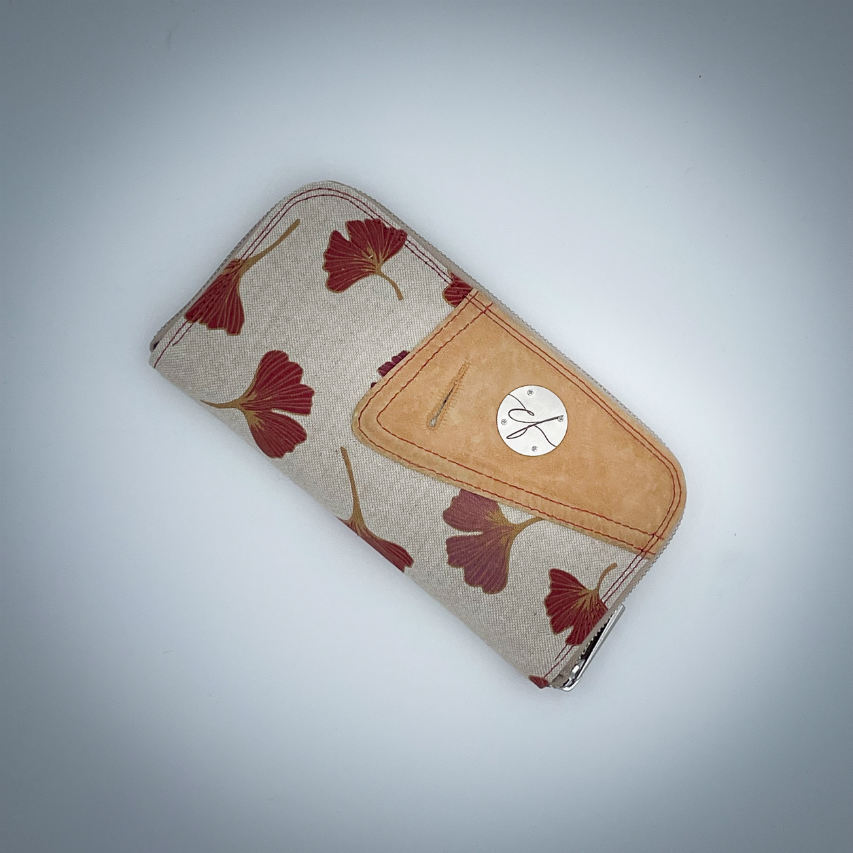 A zippered card and coin holder made with camel colored goat leather and a red Ginkgo Biloba leaves patterned polycotton canvas.