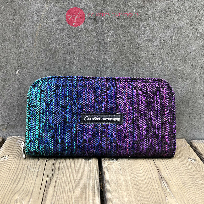 A wallet made with a babywearing wrap in a gradient from blue to violet on the outside and black, pink, and petrol poplin on the inside.