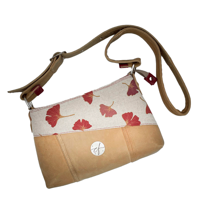 Une besace rectangulaire faite de cuir de couleur camel et d'une toile en polycoton avec un motif de feuilles de Ginkgo Biloba rouges.