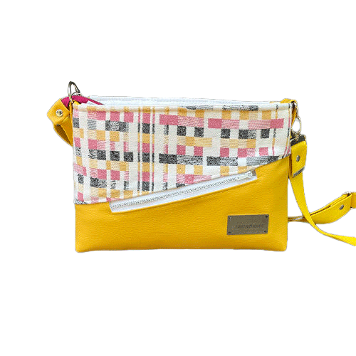 Un sac à bandoulière rectangulaire fabriqué à partir d'écharpe de portage noir, blanc, rose et jaune à motif géométrique, et de simili jaune tournesol.