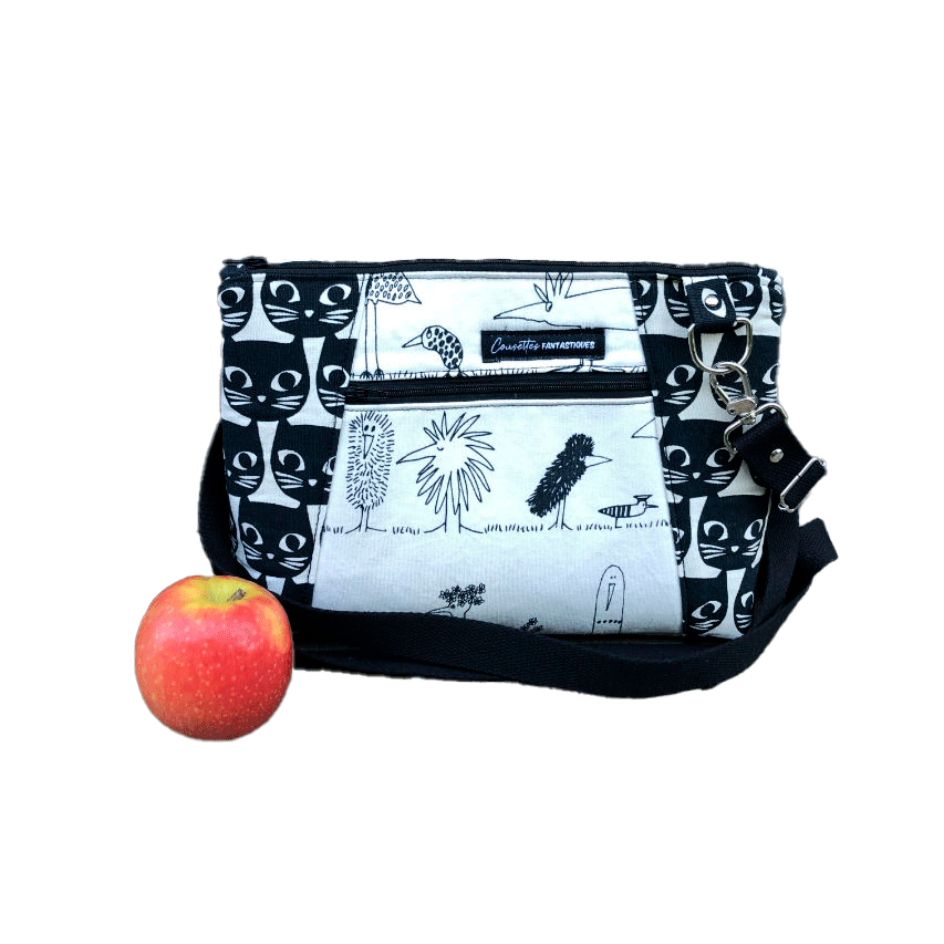 Un sac en bandoulière trapézoïdal fabriqué à partir de toile en coton noir et blanc avec des motifs stylisés de chats et d'oiseaux, assorti à de la cretonne de coton à thème aviaire à l'intérieur.