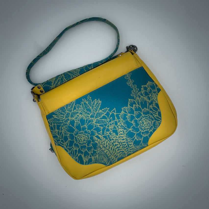 Un sac besace confectionné à partir d'écharpe de portage au motif de succulentes jaunes sur fond turquoise et d'un cuir jaune soleil, couplés à deux popelines bleu glace et jaune à l'intérieur.