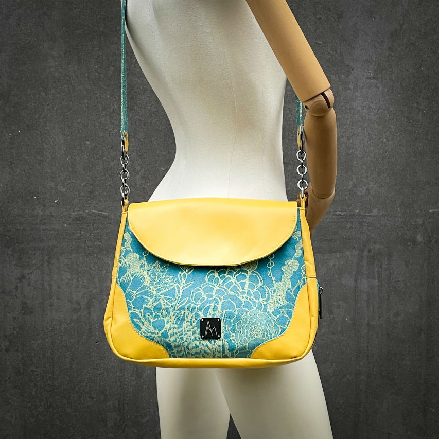 Un sac besace confectionné à partir d'écharpe de portage au motif de succulentes jaunes sur fond turquoise et d'un cuir jaune soleil, couplés à deux popelines bleu glace et jaune à l'intérieur.