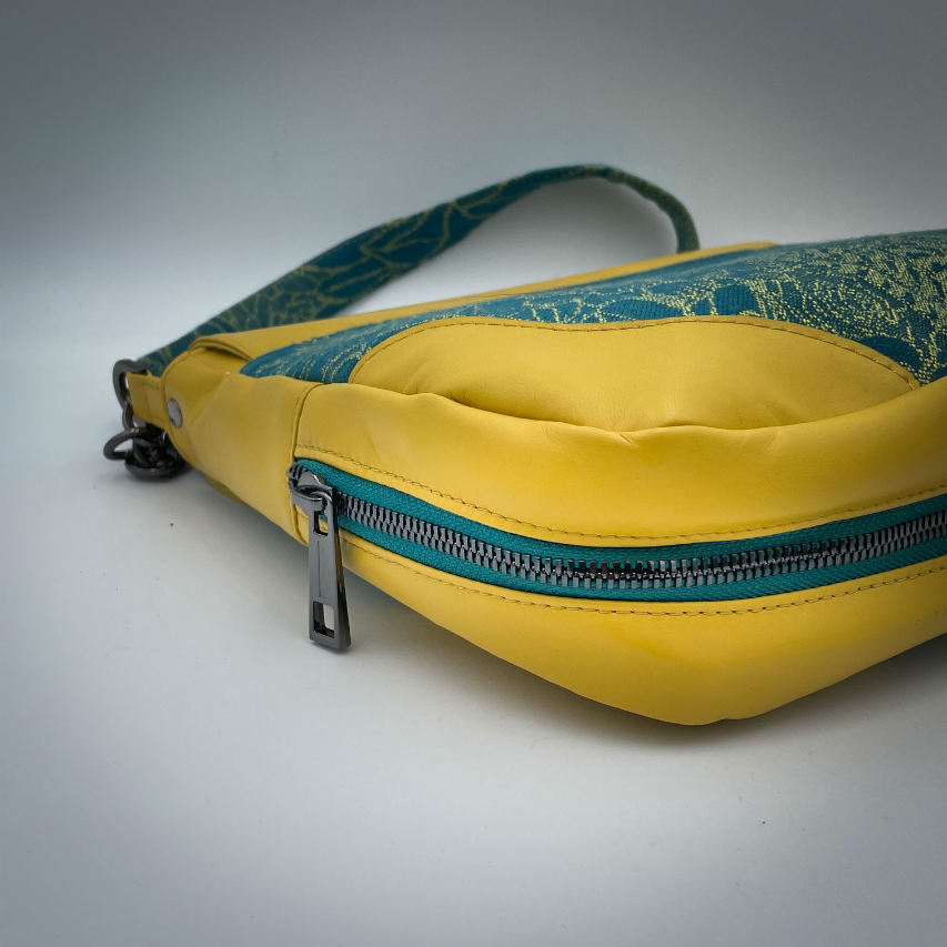 Un sac besace confectionné à partir d'écharpe de portage au motif de succulentes jaunes sur fond turquoise et d'un cuir jaune soleil, couplés à deux popelines bleu glace et jaune à l'intérieur.