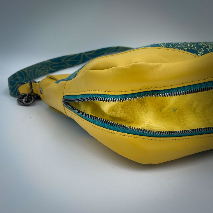 Un sac besace confectionné à partir d'écharpe de portage au motif de succulentes jaunes sur fond turquoise et d'un cuir jaune soleil, couplés à deux popelines bleu glace et jaune à l'intérieur.