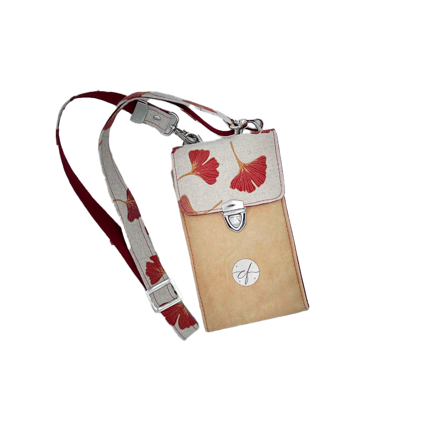 Une pochette-téléphone cousue dans un cuir de couleur camel et une toile en polycoton avec un motif de feuilles de Ginkgo Biloba rouges.