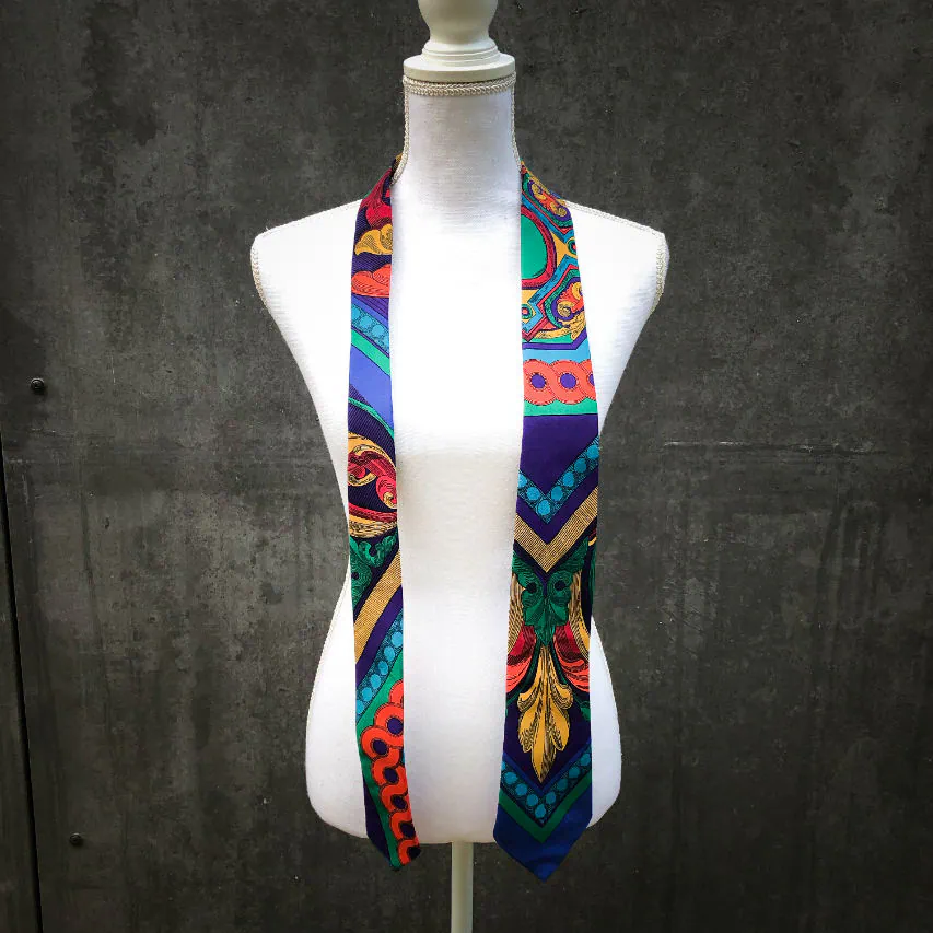 Une cravate fabriquée à partir d'un foulard de soie rouge, bleu, vert, jaune... et au motif rococco.
