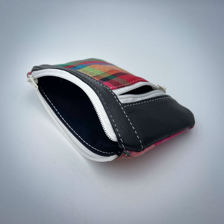 Un petit porte-monnaie zippé fabriqué à partir d'un patchwork de différents matériaux : une toile de Madras et du cuir d'agneau noir.