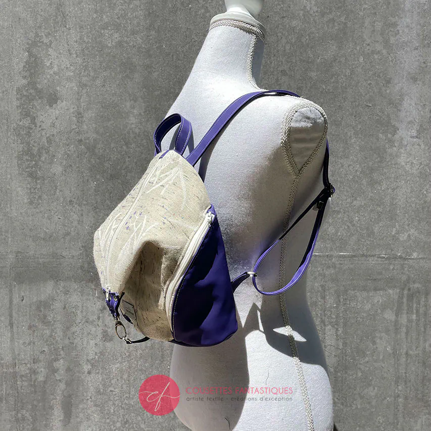 Un sac à dos confectionné en neoprene violet et en tissu d'écharpe dans des tons écru et violet, au motif d'oiseaux dans des branches.