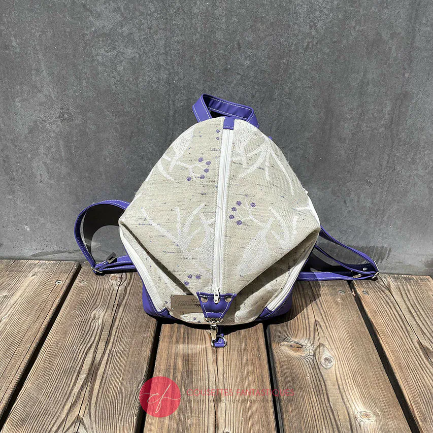 Un sac à dos confectionné en neoprene violet et en tissu d'écharpe dans des tons écru et violet, au motif d'oiseaux dans des branches.