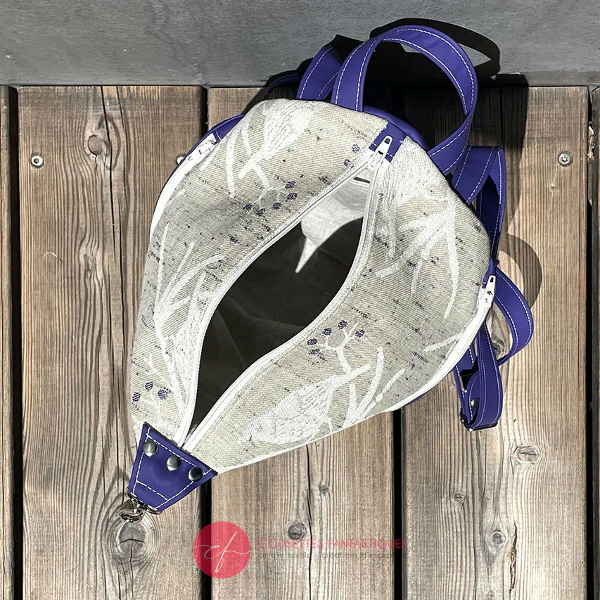 Un sac à dos confectionné en neoprene violet et en tissu d'écharpe dans des tons écru et violet, au motif d'oiseaux dans des branches.