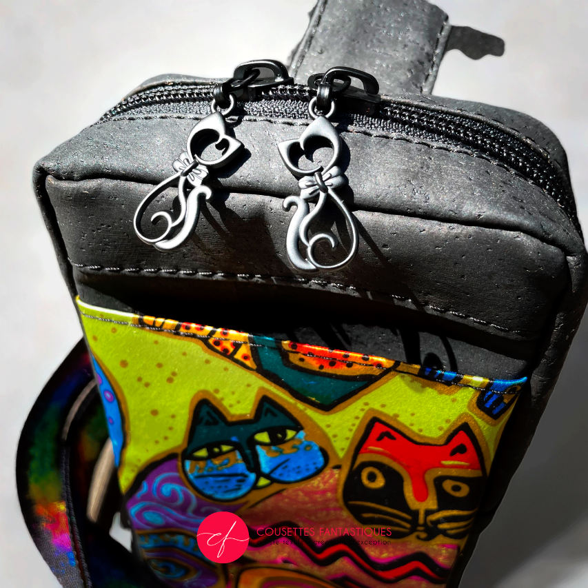 Un petit sac à dos cousu en liège noir mat et écharpe en soie avec un motif coloré de chats, associé à une sangle noire et arc-en-ciel.