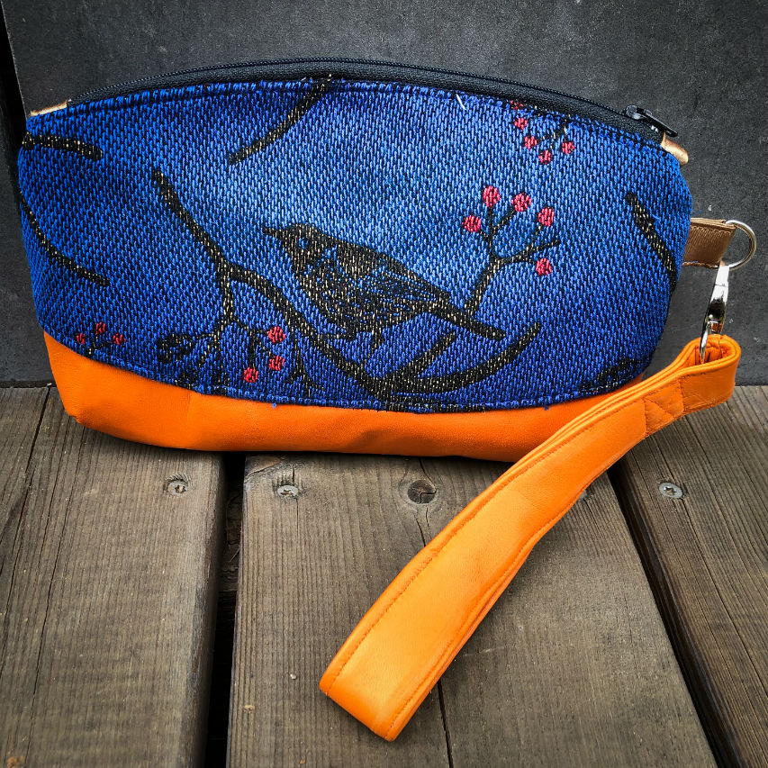 Une petite pochette zippée cousue en cuir orange et une écharpe de portage bleu électrique, noir et rouge avec un motif d'oiseaux dans des branches'.