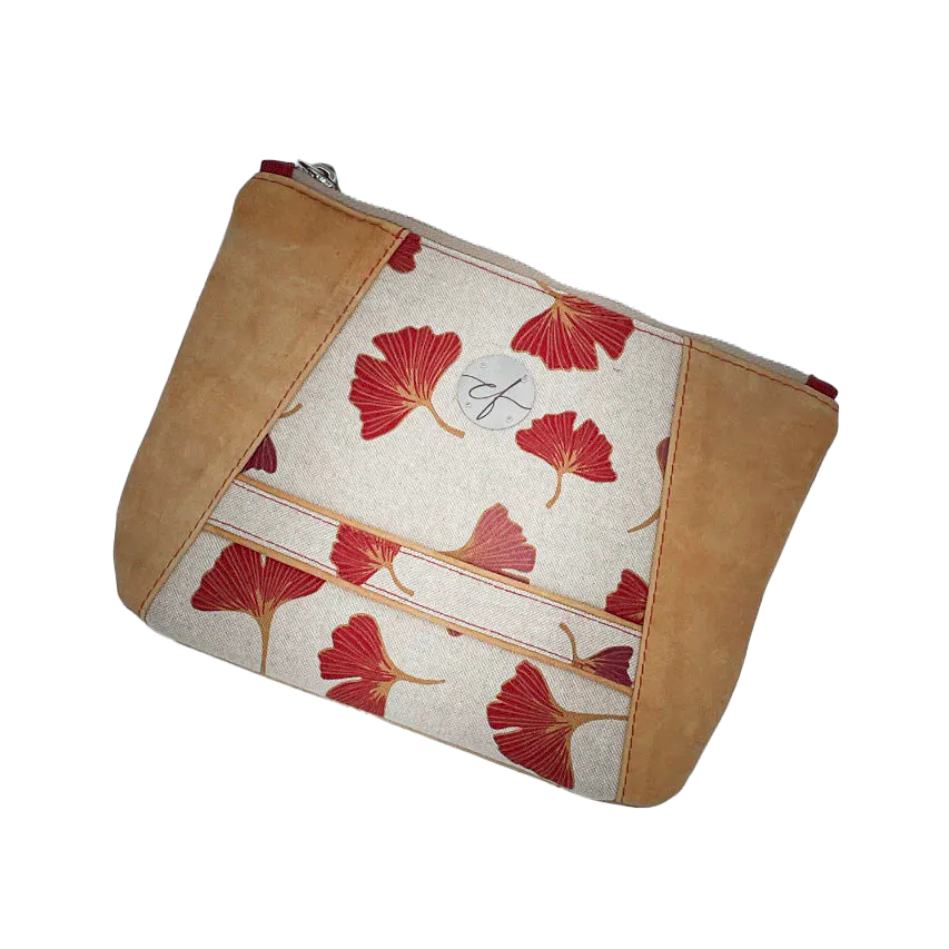 Une pochette zippée cousue dans un cuir de couleur camel et une toile en polycoton avec un motif de feuilles de Ginkgo Biloba rouges.