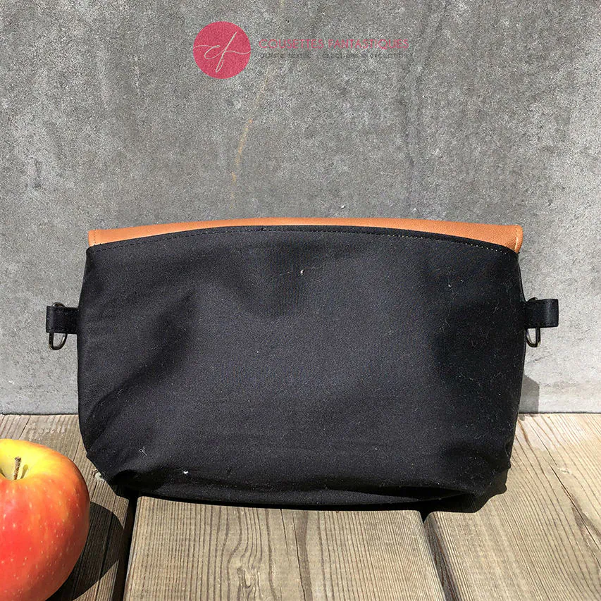 Une pochette à rabat cousue en cuir caramel, satin noir et tissu à motifs design suédois, doublée de popeline jaune.