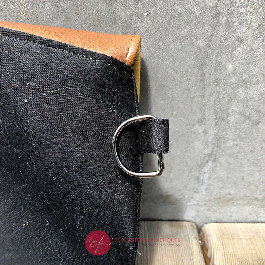 Une pochette à rabat cousue en cuir caramel, satin noir et tissu à motifs design suédois, doublée de popeline jaune.
