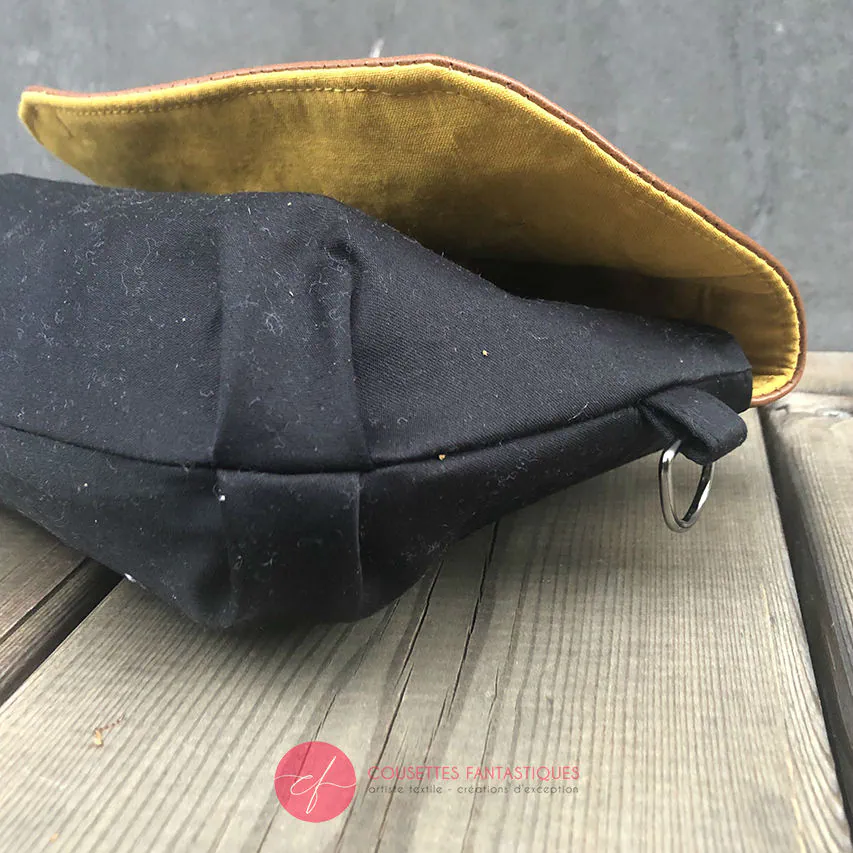 Une pochette à rabat cousue en cuir caramel, satin noir et tissu à motifs design suédois, doublée de popeline jaune.