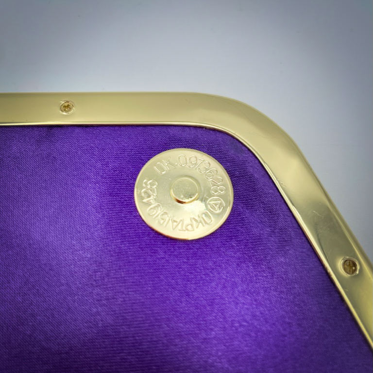 Un portefeuille fabriqué à partir de chutes de tissu provenant d'écharpes à motif géométrique violet et jaune, combinées à des simili violets et dorés à l'extérieur, et à une toile légère de lin moutarde et du satin violet profond à l'intérieur.