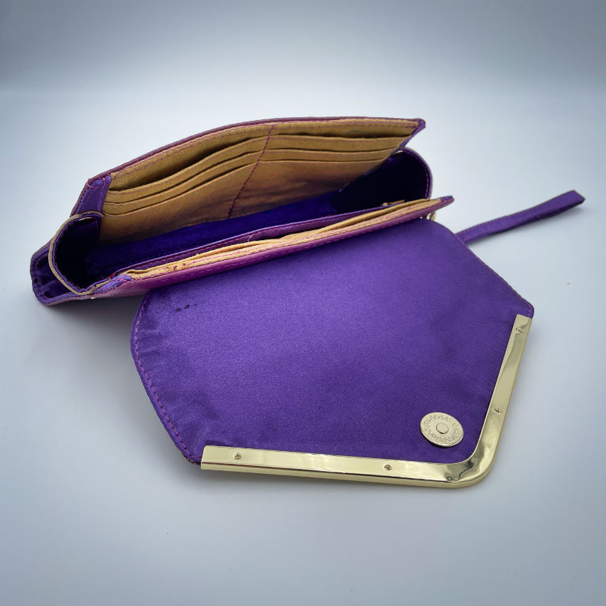 Un portefeuille fabriqué à partir de chutes de tissu provenant d'écharpes à motif géométrique violet et jaune, combinées à des simili violets et dorés à l'extérieur, et à une toile légère de lin moutarde et du satin violet profond à l'intérieur.